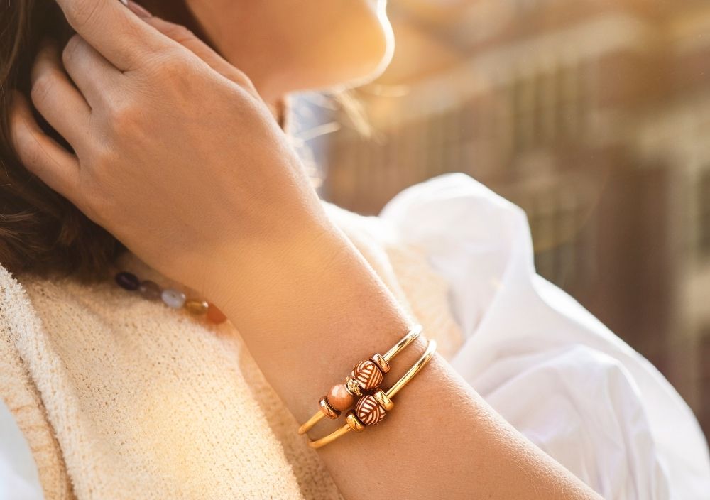 Woman wearing a gold bangle styled with barrel beads in warm sunlight.